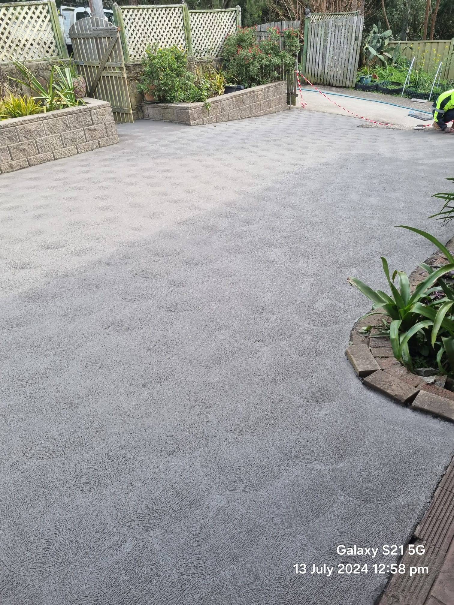 Concrete driveway framed by block retaining walls and planted beds