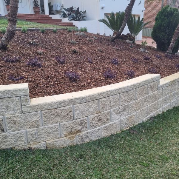 Curved sandstone block wall retaining a mulched and planted bed
