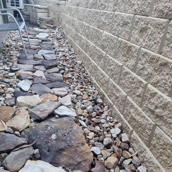 Block retaining wall beside a rock bed and stone pathway