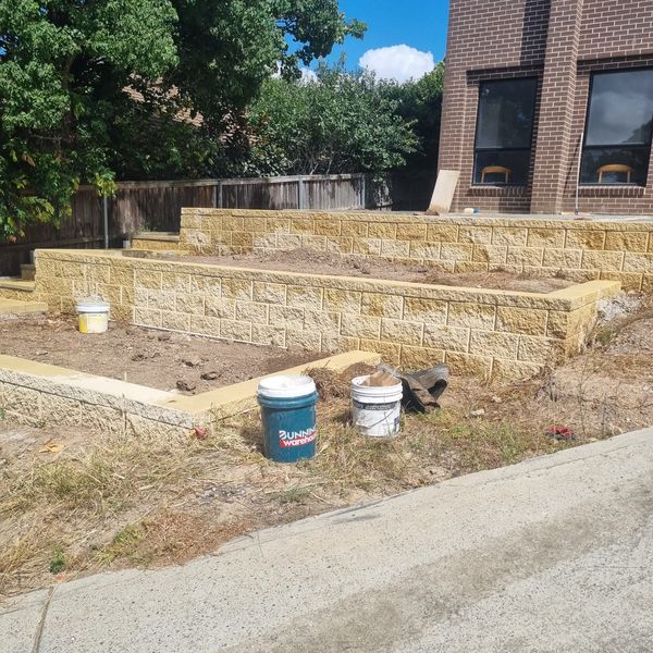 Two levels of sandstone block retaining wall holding back graded soil
