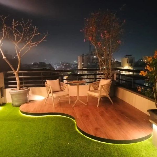 Curved timber deck and lawn on a lit rooftop terrace at night