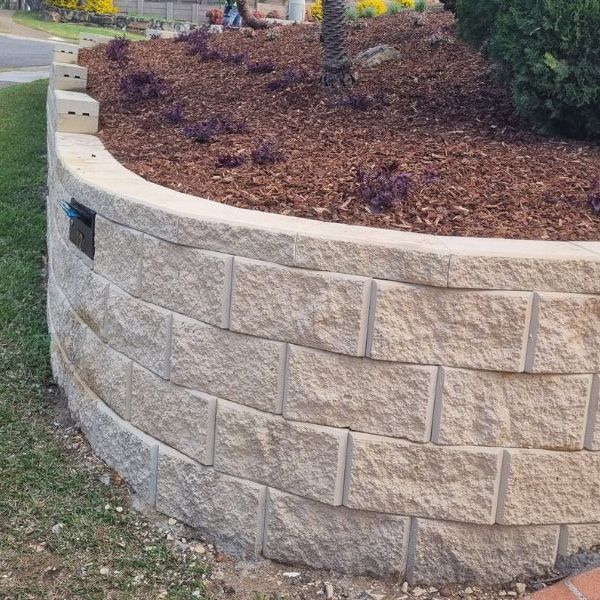 Curved sandstone block retaining wall holding a mulched garden bed