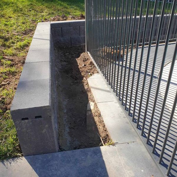 Charcoal block planter wall running beside a pool fence