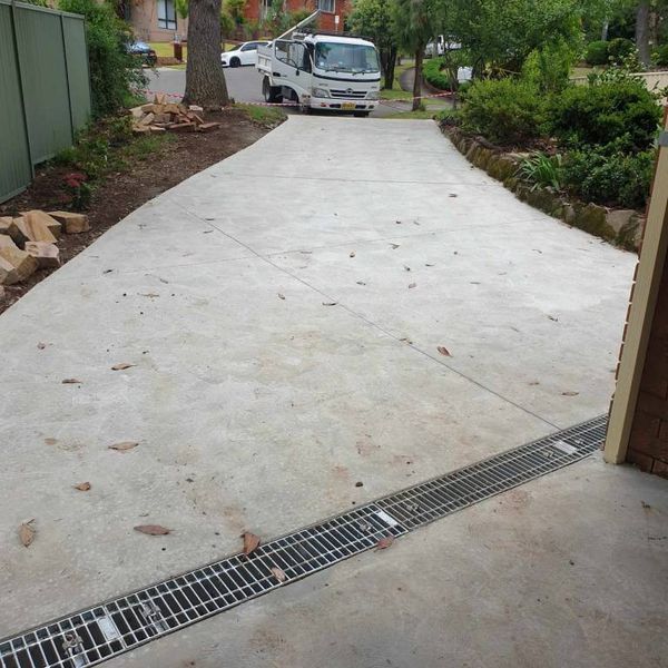Wide concrete driveway with a drainage grate across its entry