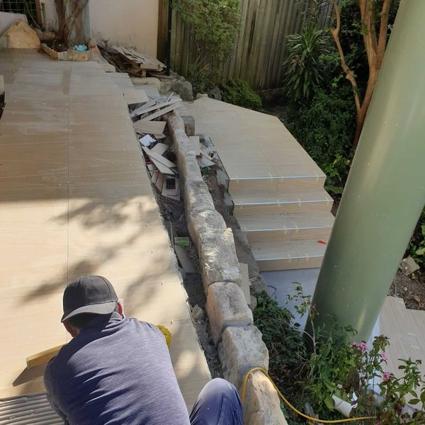 Tiled steps being laid beside a natural stone retaining wall